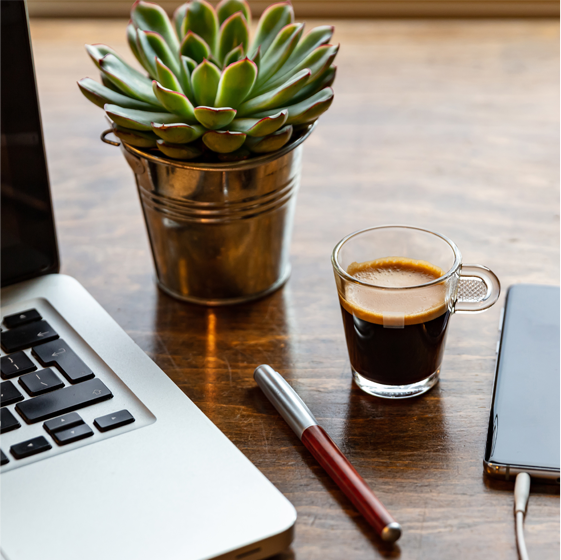 Arbeitsplatz mit Laptop, Stift, Pflanze und Kaffee